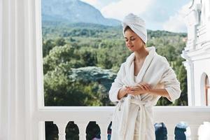 bellissimo donna con un' asciugamano su mio testa nel un' bianca accappatoio soggiorno su il balcone nel un' Hotel rilassamento concetto foto