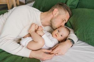 amorevole padre bugie su il letto con il suo bambino figlio, abbracci lui e baci lui foto