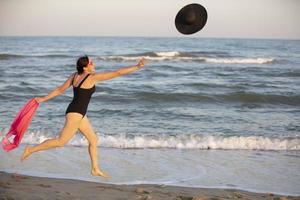 un' donna corre lungo il riva per un' cappello. vacanze a mare. foto