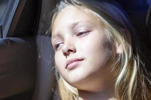 il viso di il bambino nel il macchina. bellissimo adolescente ragazza illuminato di il sole nel trasporto. stanco passeggeri. foto