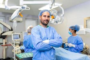 ritratto di maschio chirurgo in piedi con braccia attraversato nel operazione Teatro a Ospedale. squadra chirurghi siamo l'esecuzione un operazione, mezzo anziano medico è guardare a telecamera, nel un' moderno operativo camera foto