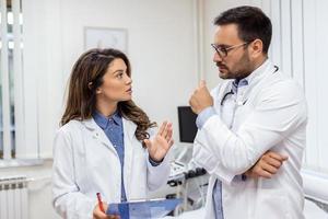 fiducioso medici discutere al di sopra di medico grafico. maschio e femmina assistenza sanitaria lavoratori siamo indossare laboratorio cappotti. essi siamo Lavorando nel Ospedale. foto