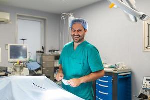 ritratto di maschio chirurgo nel operazione Teatro guardare a telecamera mostrando ok gesto. medico nel scrub e medico maschera nel moderno ospedale operativo camera. foto