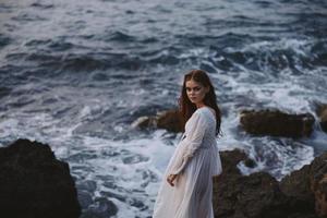 donna nel bianca vestito sta su un' scogliera stile di vita pietra costa paesaggio inalterato foto