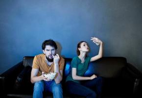 emotivo donna e uomo con un' piatto di Popcorn Guardando tv nel il sera in casa foto