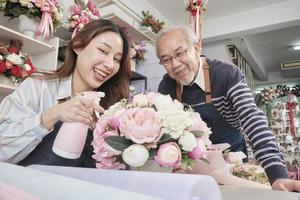 vecchio uomo e giovane bellissimo asiatico femmina fioraio lavoratori acqua spruzzatura un' flora mazzo insieme, contento opera nel un' colorato fiore negozio negozio, fresco fioritura mazzi di fiori decorare, pmi attività commerciale imprenditore. foto