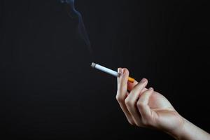 mano femminile che tiene una sigaretta fumante su uno sfondo scuro con spazio di copia foto