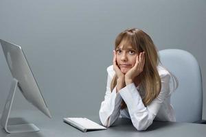 annoiato bella bionda donna d'affari lavoratore libero professionista utilizzando del desktop computer seduta a posto di lavoro nel grigio moderno ufficio. a distanza lavoro, tecnologia e carriera professione concetto. copia spazio foto