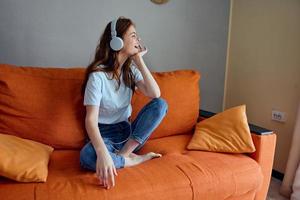 donna ascoltando per musica con cuffie su il arancia divano stile di vita foto