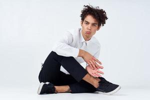 giovane uomo con Riccio capelli si siede a gambe incrociate su il pavimento foto