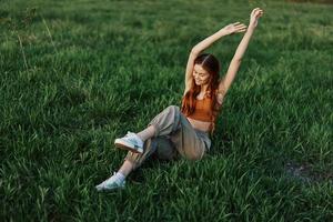 un' donna bugie su il verde erba nel il parco con sua gambe su e avendo divertimento contro il prato, visto a partire dal sopra. il concetto di rilassante nel natura e cura per il ambiente foto