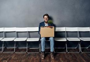 uomo si siede su un' sedia scatola con cose licenziamento malcontento depressione foto
