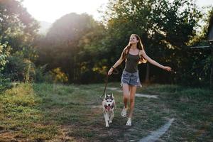 un' donna corre con un' cane nel il foresta durante un sera camminare nel il foresta a tramonto nel autunno. stile di vita gli sport formazione con il tuo Amati cane foto