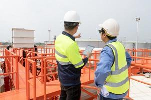 Due pesante industriale ingegneri in piedi nel un' standard acqua trattamento pianta uso digitale tavoletta computer e chattare. asiatico industria professionisti foto