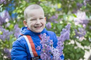 un' bambino nel un' lilla. ridendo ragazzo con un' mazzo di primavera fiori. foto