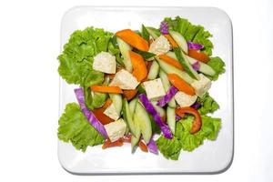 fresco verde verdura insalata nel un' piatto. salutare peperone, carota, formaggio, pomodoro e lattuga pasto su bianca sfondo foto
