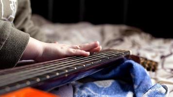 la mano del bambino sul collo di una chitarra acustica di colore arancione, imparando a suonare lo strumento foto