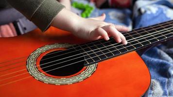 la mano del bambino tocca le corde di una chitarra acustica a sei corde, guadagnando per suonare uno strumento musicale foto