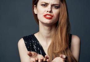 un' donna nel un' nero vestito con rosso labbra gesti con sua mani perplesso Guarda grigio sfondo foto