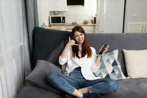 allegro donna parlando su il Telefono seduta su il divano riposo nel il appartamento foto