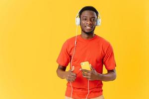 uomo di africano aspetto nel cuffie con un' Telefono nel il suo mani nel tecnologia studio giallo sfondo foto