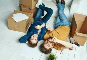 uomini e donne menzogna su il pavimento in casa con scatole di documenti di fiori nel un' pentola in movimento foto