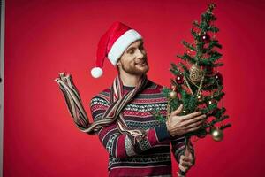 un' uomo nel un' Santa cappello Natale albero decorazione giocattoli rosso sfondo foto