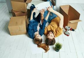 uomini e donne menzogna su il pavimento in casa con scatole di documenti di fiori nel un' pentola in movimento foto