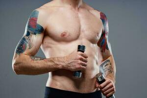 maschio atleta con un' tatuaggio su il suo braccio nudo torso gonfiato muscoli manubri fitness foto