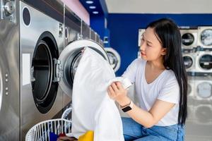 giovane asiatico casalinga è soddisfatto con bianca Abiti dopo lavaggio macchina finiture opera nel lavanderia negozio. foto