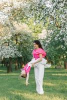 un' giovane bellissimo madre è contento e Tenere sua figlia nel sua braccia, essi siamo avendo divertimento nel il primavera parco foto