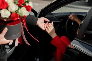 uomo gentile con un mazzo di fiori, aiutando una donna d'affari in un abito rosso per uscire da un parcheggio all'aperto foto