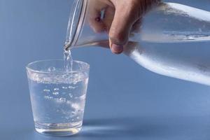 bicchiere di acqua essere pieno su blu sfondo foto