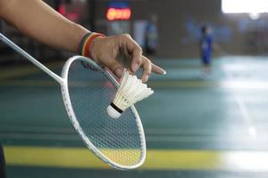 badminton giocatore indossa arcobaleno braccialetti e Tenere racchetta e bianca volano nel davanti di il netto prima servendo esso per giocatore nel un altro lato di il Tribunale, concetto per lgbt persone attività. foto