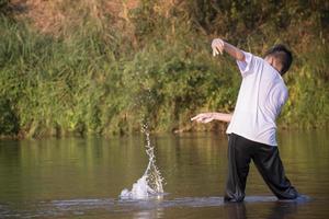 asiatico ragazzo è la spesa il suo tempi liberi di immersione, nuoto, lancio rocce e attraente pesce nel il fiume felicemente, passatempo e felicità di bambini concetto, nel movimento. foto