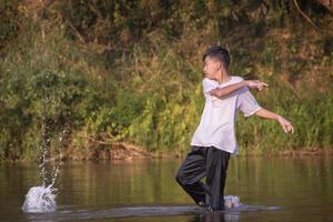 asiatico ragazzo è la spesa il suo tempi liberi di immersione, nuoto, lancio rocce e attraente pesce nel il fiume felicemente, passatempo e felicità di bambini concetto, nel movimento. foto