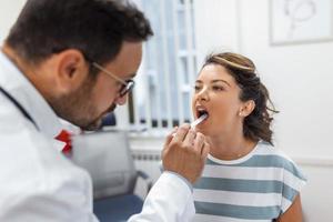 medico utilizzando ispezione spatola per esaminare paziente gola. ent medico fare gola esame di un' donna. paziente ha aperto sua bocca per gola verifica foto