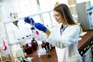 giovane scienziato femminile esaminando liquido nel laboratorio biochimico foto