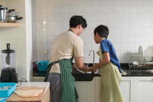 contento sorridente giovane asiatico padre e figlio lavaggio piatti nel cucina a casa foto