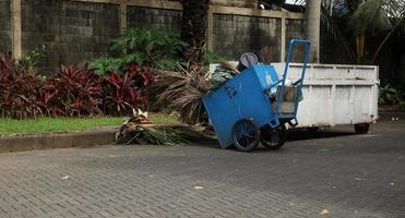 uno blu Tirare spazzatura carrello con ruote. gerobak sampa biru fotografia oggetto all'aperto isolato su minuscolo giardino e mattone terra pavimentazione sfondo. foto