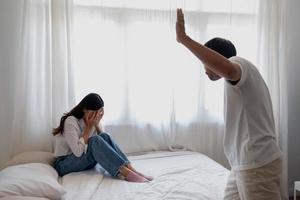 interno violenza. famiglia conflitto uomini attacco e battere donne a casa. spaventato donna copertura sua viso seduta su il letto. lei era impaurito. foto