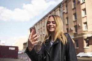 alla moda donna indossare pelle giacca all'aperto vicino il edificio bionda fresco aria foto