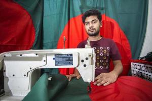 bangladesh, dicembre 09, 2017, md sfocato ahimè, un' giovane sarto spende un' occupato tempo fabbricazione bangladeshi nazionale bandiere avanti di vittoria mese vicino gulistan, dacca. foto