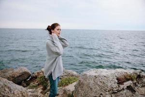 donna nel un' grigio maglione sta su un' roccioso riva natura rilassamento concetto foto
