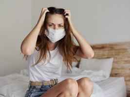 donna nel quarantena tocchi sua testa con sua mani e si siede su il letto viaggio modello coronavirus foto