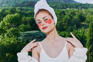 donna nel un' accappatoio con un' asciugamano su il suo testa cerotti su il suo viso sta su il balcone inalterato foto