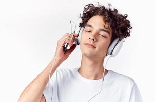 emotivo uomo con Riccio capelli e nel cuffie ascolta per musica leggero sfondo foto