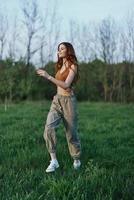 un' giovane donna nel un' superiore e verde pantaloni e atletico scarpe da ginnastica è jogging su il estate verde erba con sua capelli perdere foto