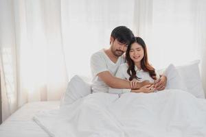 contento giovane asiatico coppia abbracciando, dispettoso, giocando allegramente nel letto a casa, romantico tempo per migliorare famiglia legame. famiglia concetto. foto