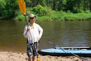 un' uomo con un' kayak pagaia per rafting sta su il fiume banca. sport acqua escursione, un' estate avventura. eco-friendly e estremo turismo, attivo e salutare stile di vita foto